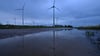 Windräder spiegeln sich in der Morgendämmerung auf in einer Pfütze am Windpark bei Westhausen.