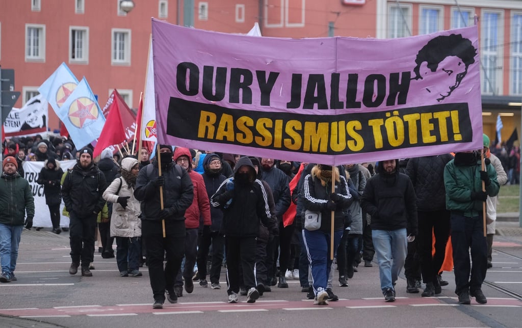 Teilnehmer einer linken Demonstration gehen mit Transparenten und Fahnen am 7. Januar 2024 durch Dessau-Roßlau.