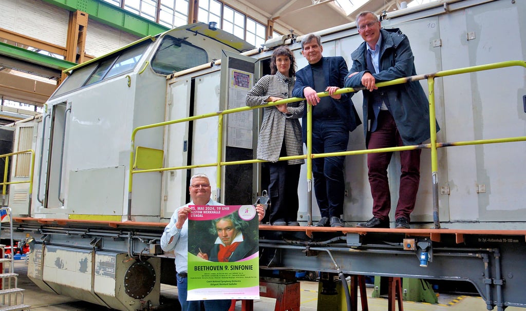 Alstom-Vertriebsleiter Stefan Heinzmann (von links), Schauspielerin Friederike Becht, Festspiel-Intendant Reinhard Seehafer und Festspiel-Geschäftsführer Michael Pohl werben in der Lok-Halle des Stendaler Alstom-Werkes für das Konzert am 25. Mai 2024 in eben dieser Werkhalle.