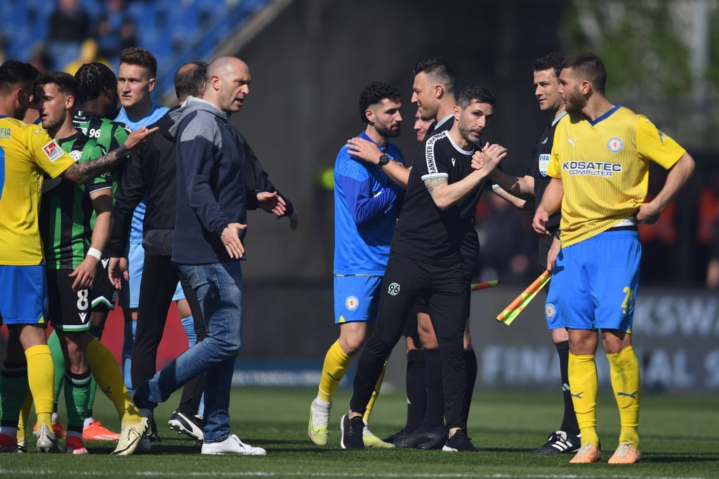 Hannovers Trainer Stefan Leitl (3.v.r) und Braunschweigs Trainer Daniel Scherning stehen nach dem Schlusspfiff auf dem Feld.