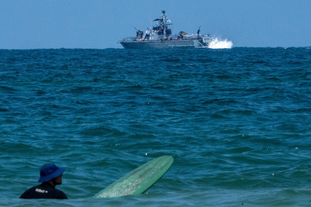 Ein Surfer wartet auf eine Welle, während ein israelisches Marineschiff im Mittelmeer vor der Küste von Hadera patrouilliert.