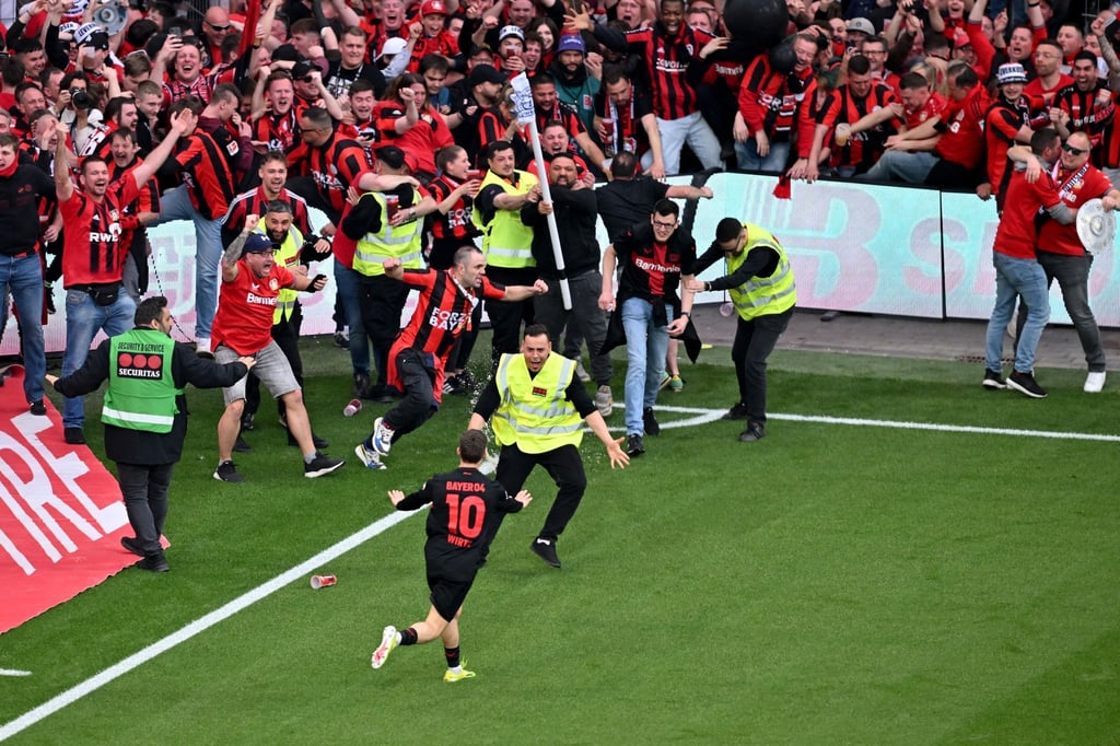 Fußball: Bundesliga, Bayer 04 Leverkusen - SV Werder Bremen, 29. Spieltag, BayArena. Leverkusens Florian Wirtz (vorne M, #10) dreht nach seinem Tor zum 4:0 jubelnd ab und beruhigt Fans und Sicherheitspersonal, die auf das Spielfeld laufen.