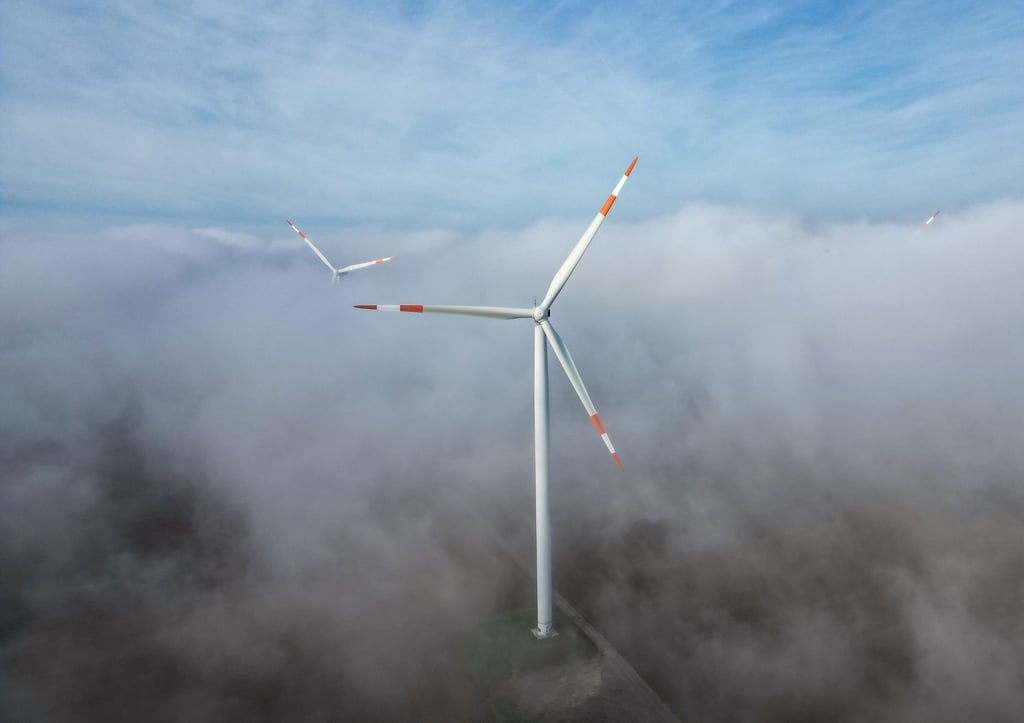 Die Windräder in einem Windpark ragen aus dem Morgennebel hervor.