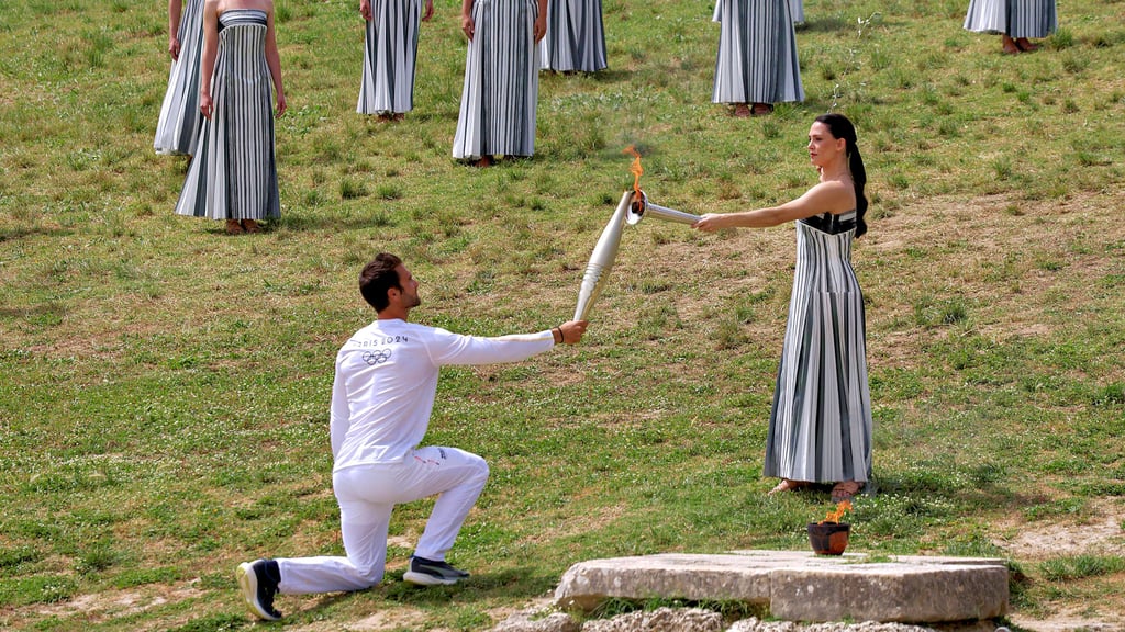 Ruder-Olympiasieger Stefanos Ntouskos erhält die Flamme von der griechischen Schauspielerin Mary Mina, die die Hohepriesterin spielt. Ntouskos ist der erste Fackelläufer auf dem Weg zur Eröffnung der Sommerspiele in Paris.