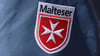 Das Logo der Malteser ist an der Jacke eines Helfers zu sehen.