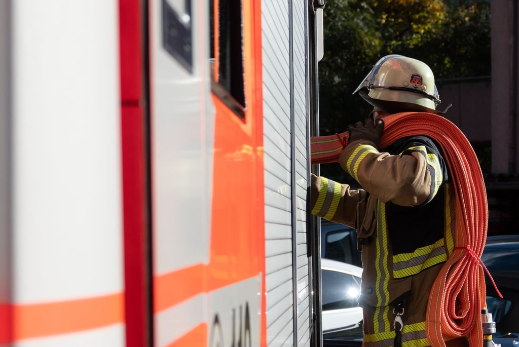 Eine Einsatzkraft der Feuerwehr nimmt einen Schlauch aus einem Einsatzfahrzeug der Feuerwehr.