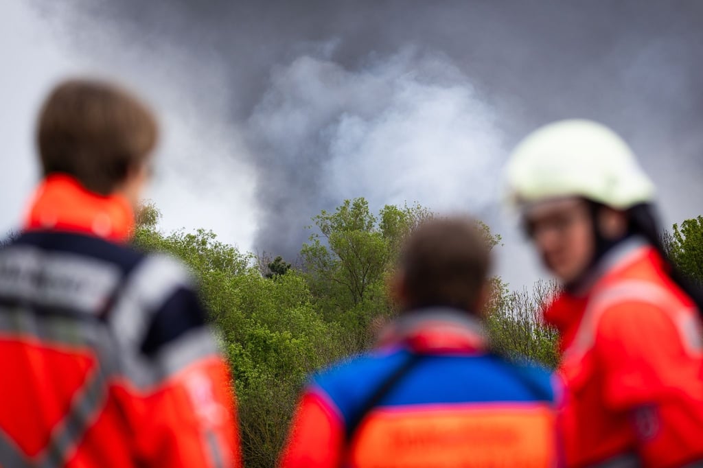 Einsatzkräfte der Feuerwehr stehen bei einem Großbrand in einem Braunschweiger Industriegebiet.
