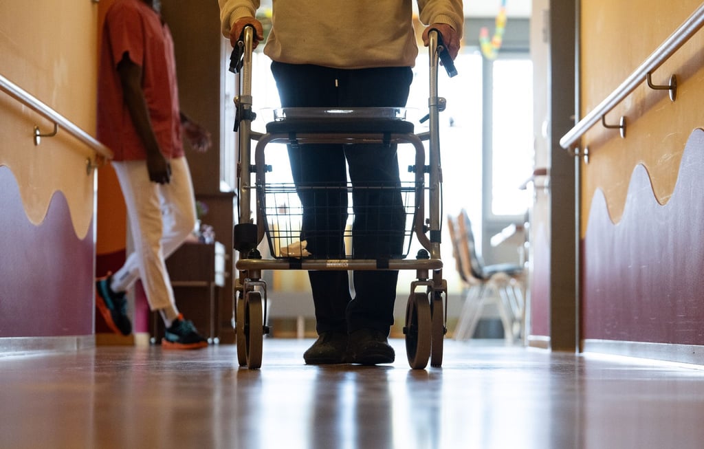 Ein Bewohner eines Pflegeheims geht mit einem Rollator einen Gang entlang.