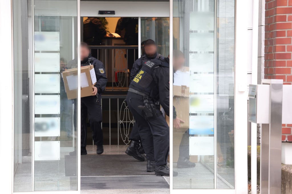 Polizeibeamte tragen in Kartons sichergestelltes Material aus einem Gebäude.