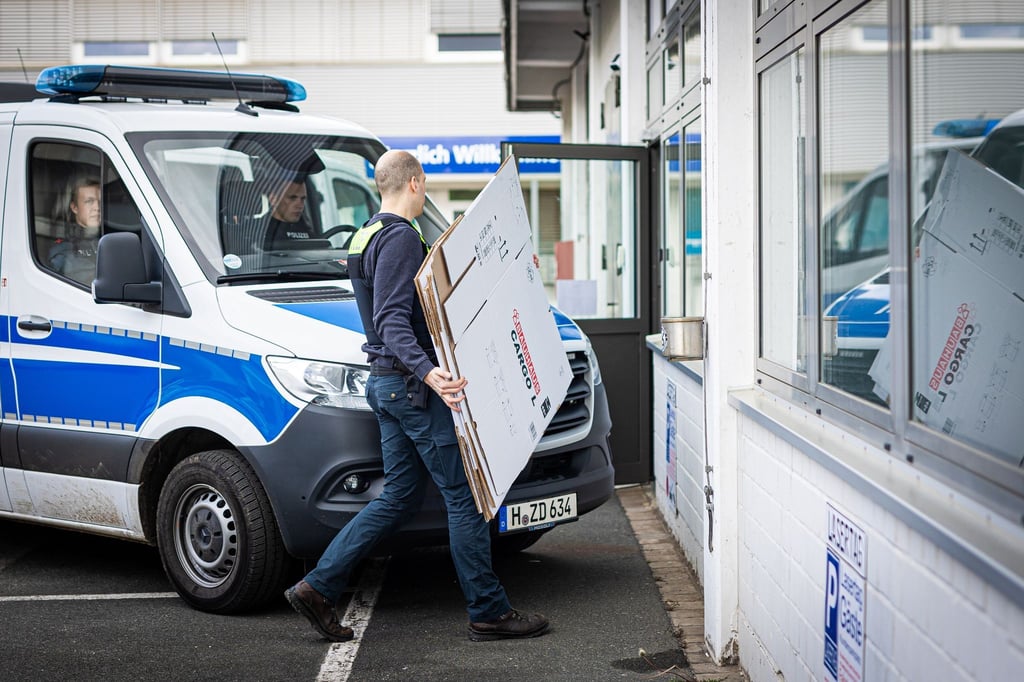 Ein Polizeibeamter geht während einer Durchsuchung an einem Polizeiwagen vorbei.