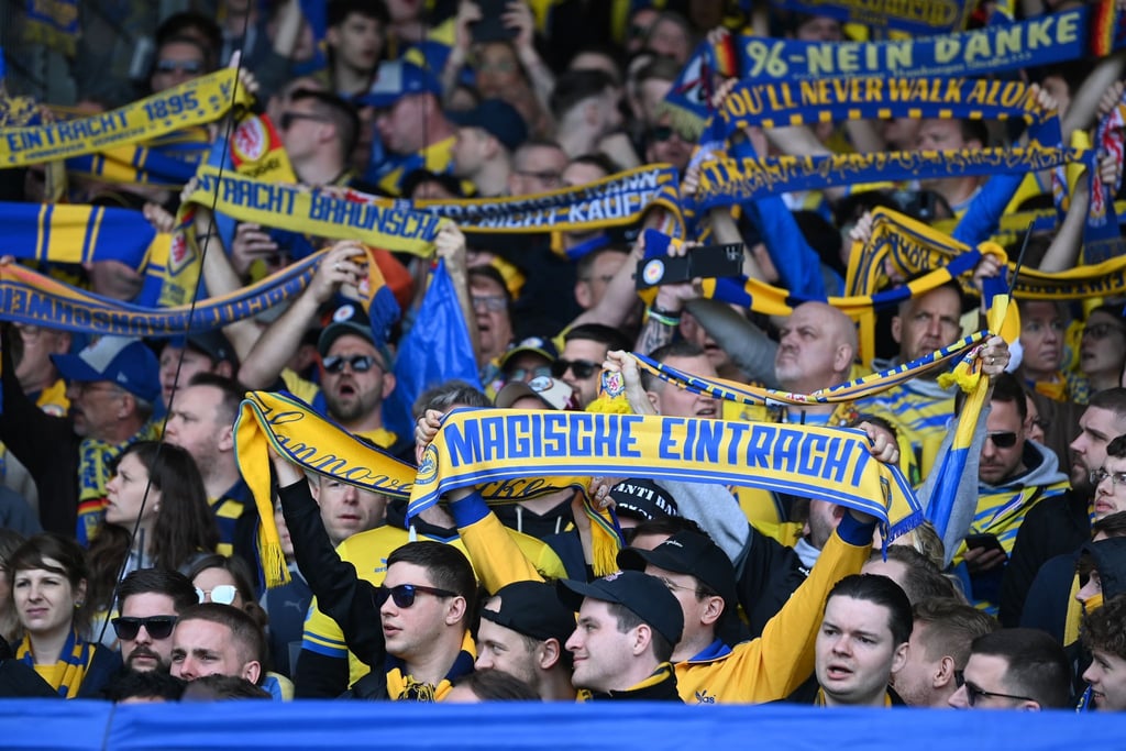 Braunschweiger Fans stehen mit ihren Schals auf der Tribüne.