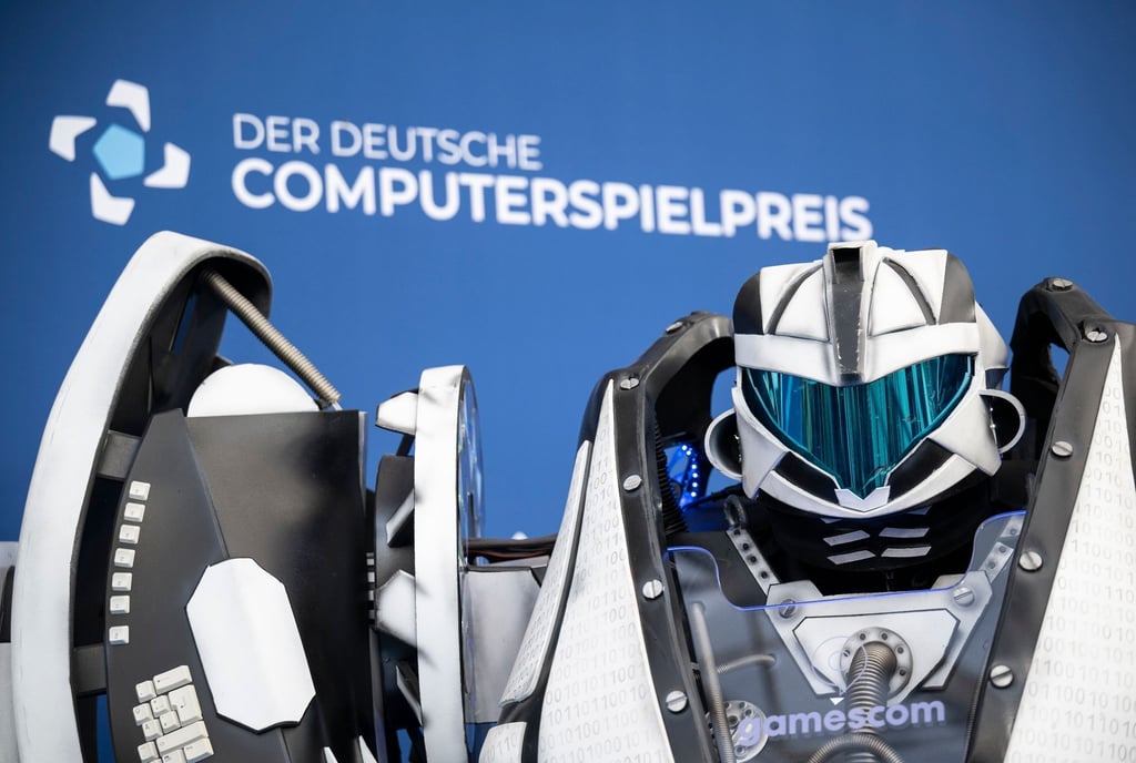 Der Gamescom Bot steht vor der Fotowand mit Schriftzug „Der Deutsche Computerspielpreis“.