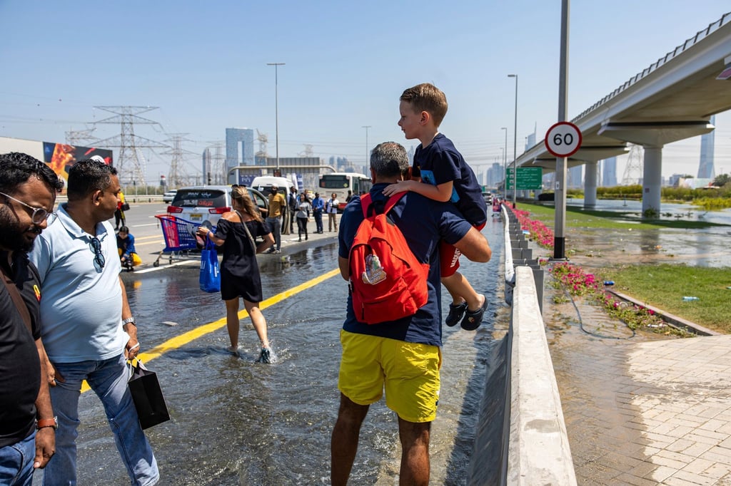 Ein Mann trägt ein Kind durch das von starkem Regen verursachte Hochwasser in Dubai.