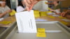 Ein Stimmzettelumschlag für die Briefwahl wird in eine Wahlurne geworfen.