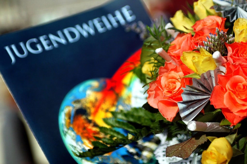 Eine Jugendweihe-Urkunde liegt in der Stadthalle in Burg neben einem Blumenstrauß.