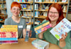 Die Mitarbeiterinnen der Stadtbibliothek Anika Mlenek (li.) und Christiane Lehmann zeigen einige der auffällig gestalteten „New Adult“-Romane, die beim jungen Publikum gefragt sind. 