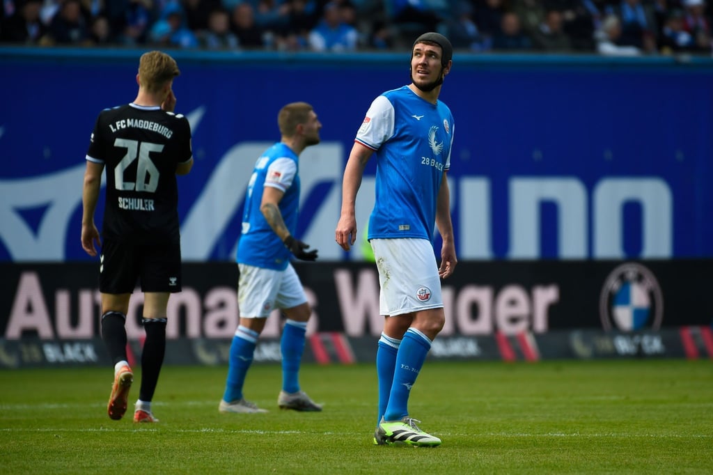 Rostocks Damian Roßbach (r) schaut während einer Spielunterbrechung auf die Anzeigentafel.