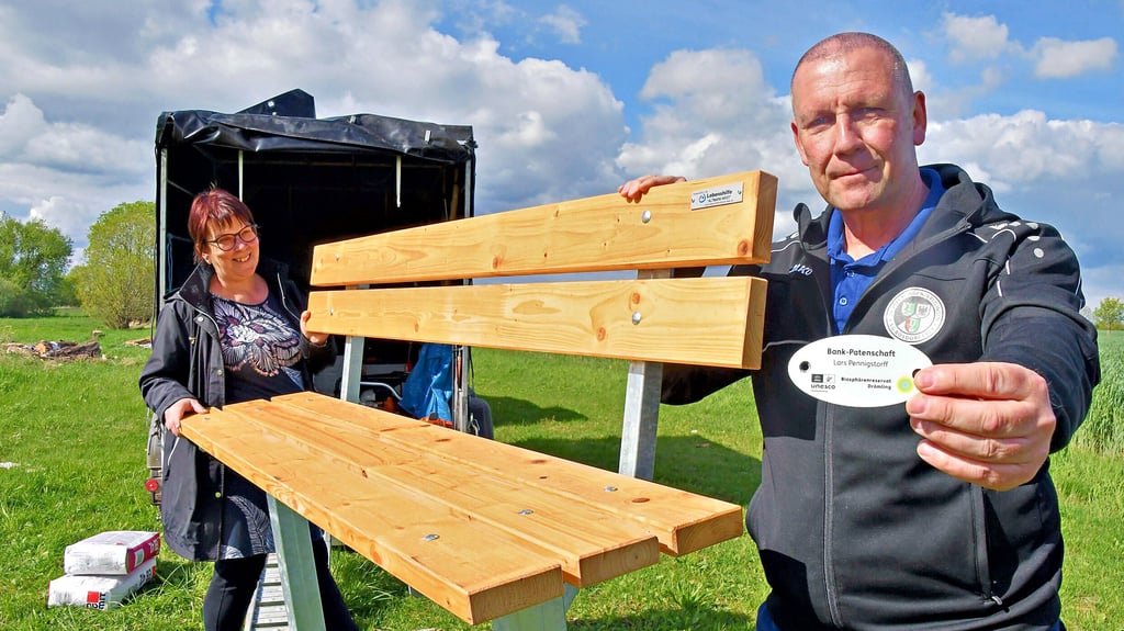 Stolz zeigt Lars Pennigstorff das Schildchen, auf dem zu lesen ist, dass er die Bank-Patenschaft übernommen hat. „Auch diese Bank wurde von unseren Freunden des Reservates in der Werkstatt der Lebenshilfe Altmark-West in Gardelegen gebaut“, erklärt Sabine Wieter vom Reservat und hilft beim Bankaufstellen.