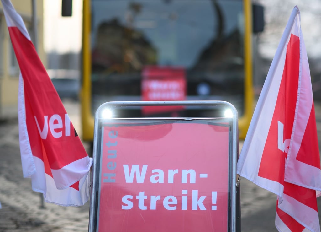Ein Schild „Warnstreik“ steht vor einem Bus der Dresdner Verkehrsbetriebe (DVB).