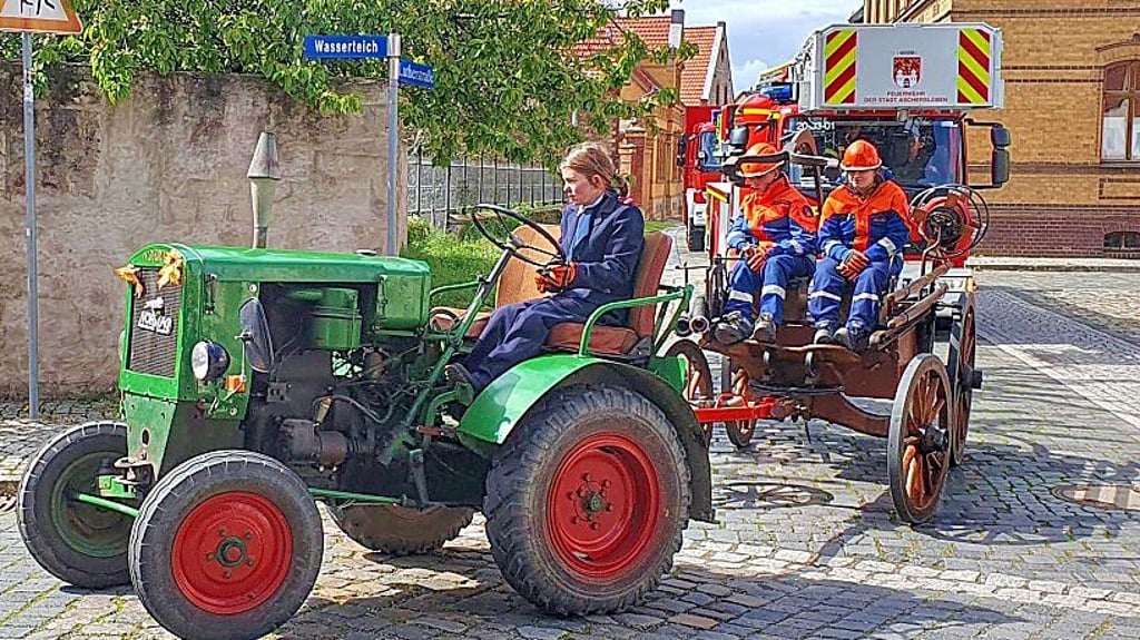 Mit einem alten Trecker wird die noch ältere Feuerwehrspritze, auf der Jugendfeuerwehrmitglieder sitzen, durch das Dorf gezogen.