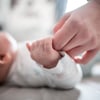Ein Baby klammert sich an den Finger seiner Mutter. (Foto: Fabian Strauch/dpa)