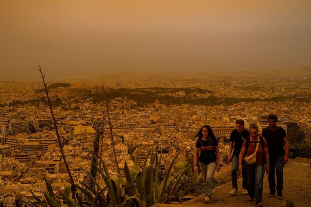 Touristen spazieren auf dem Lycabettus-Hügel, während der Himmel über Athen mit dem antiken Akropolis-Hügel im Hintergrund infolge von Saharastaub eingetrübt ist.