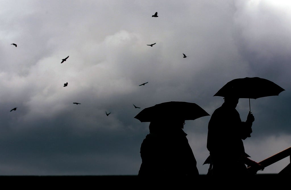 Passanten gehen mit Regenschirmen durch eine Stadt.