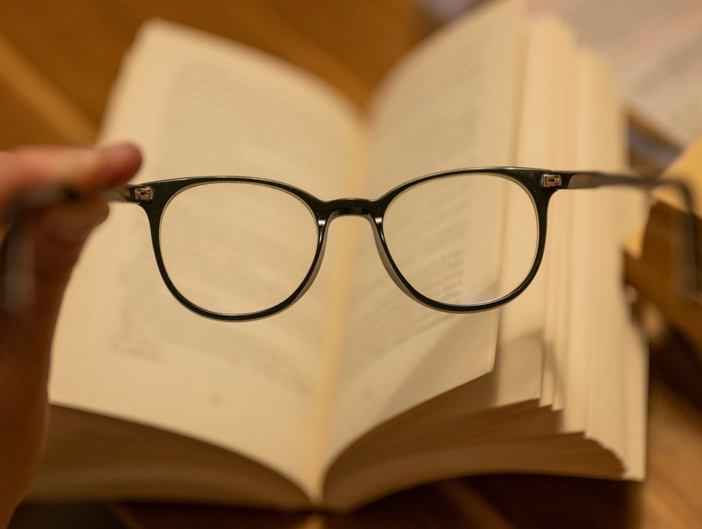 Ein Mann hält eine Lesebrille vor einem geöffneten Papierbuch.