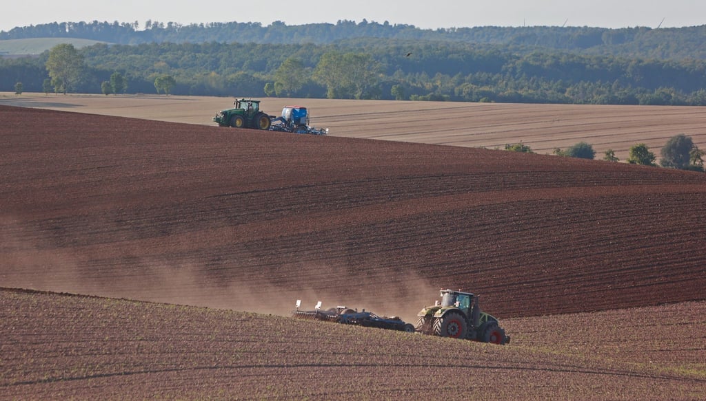 Ein Landwirt fährt mit einem Traktor über ein Feld und lockert den Boden auf.