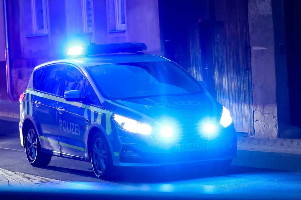 Ein Fahrzeug der Polizei fährt mit Blaulicht am Abend durch eine enge Straße.