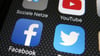 Die Icons der Plattformen Facebook, Twitter und YouTube sind auf dem Display eines Smartphones zu sehen.