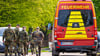 Soldaten der Bundeswehr gehen eine Straße in einem Wohngebiet entlang, vorbei an einem Einsatzfahrzeug der Feuerwehr.