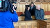Der Angeklagte (r) steht vor Beginn des Prozesses mit seinem Anwalt Temba Hoch (hinten) und einer Dolmetscherin im Gerichtssaal im Landgericht Bremen.