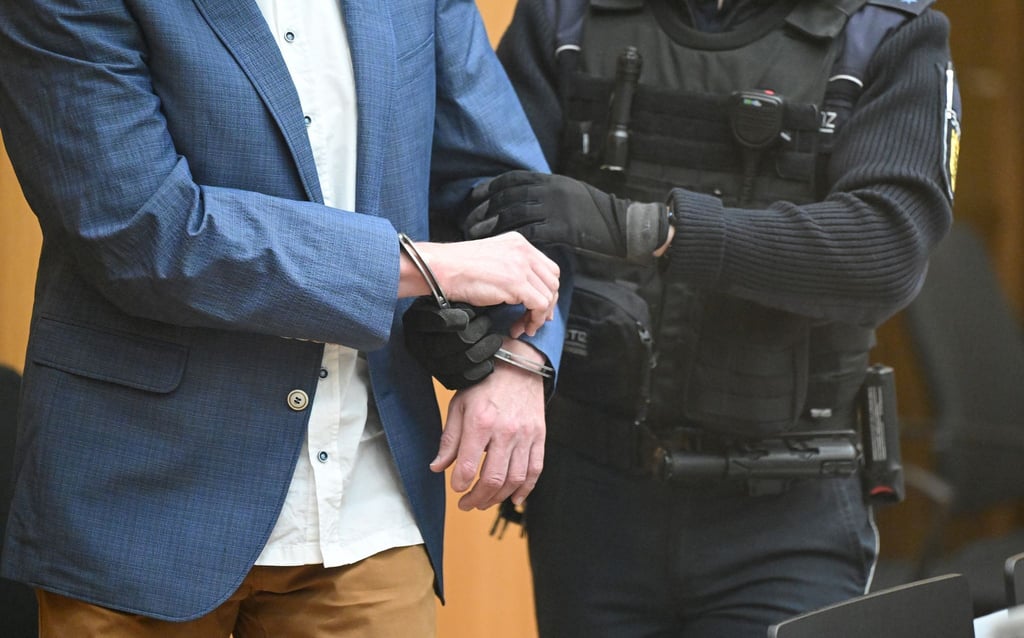 Ein Angeklagter wird bei Prozessbeginn in den Gerichtssaal geführt.