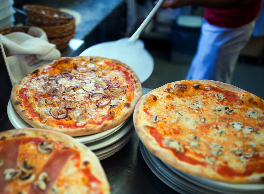 In einer Pizzeria liegen fertige Pizzen auf Tellern.