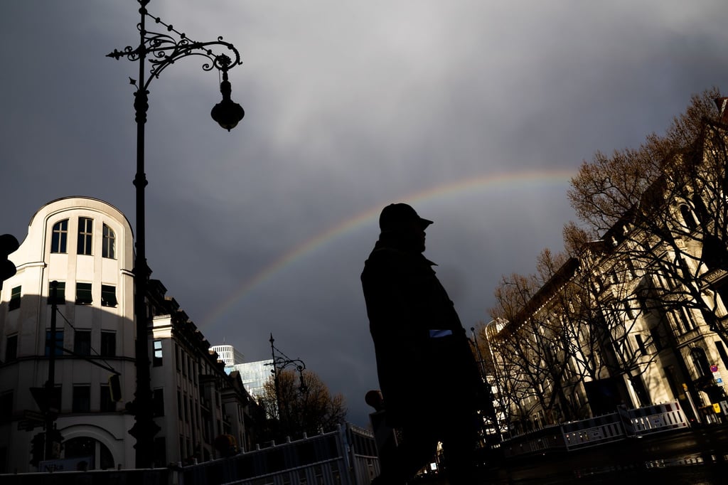 Ein Mann überquert unter einem Regenbogen den Kurfürstendamm.