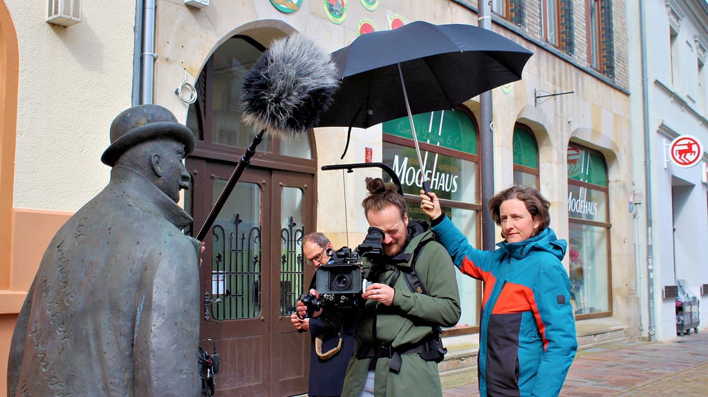 Kameramann Felix Abraham (Mitte) setzt die Reutterstatue in Gardelegens Innenstadt ins Bild. Zusammen mit Eike Goreczka (links), Helen Hahmann (rechts) und Claus Störmer (nicht im Bild) hat er für einen Film über Otto Reutter in der Stadt gedreht. Das Team hat auch die Otto-Reutter-Grundschule besucht.