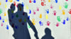 Ein Mann mit einem Kind auf dem Arm und einem an der Hand wirft einen Schatten auf eine mit bunten Handabdrücken bemalte Wand.