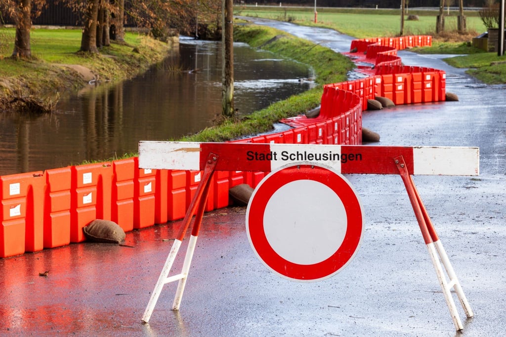 Eine Absperrung steht neben einem mobilen Damms, der Anwohner des Ortsteils Rappelsdorf vor dem Fluß Schleuse schützen soll.