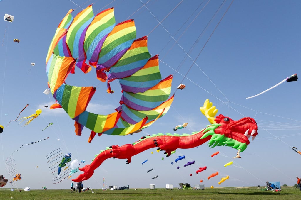 Zahlreiche bunte Flugdrachen schweben beim Drachenfest in der Luft.