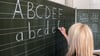 Eine Grundschullehrerin schreibt die ersten Buchstaben des Alphabets auf eine Schultafel in einem Klassenzimmer.