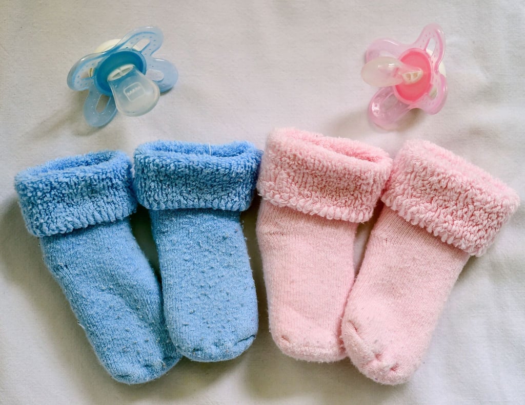 Rosa und blaue Söckchen und dazu die farbigen Nuckel liegen in einem Babybett.