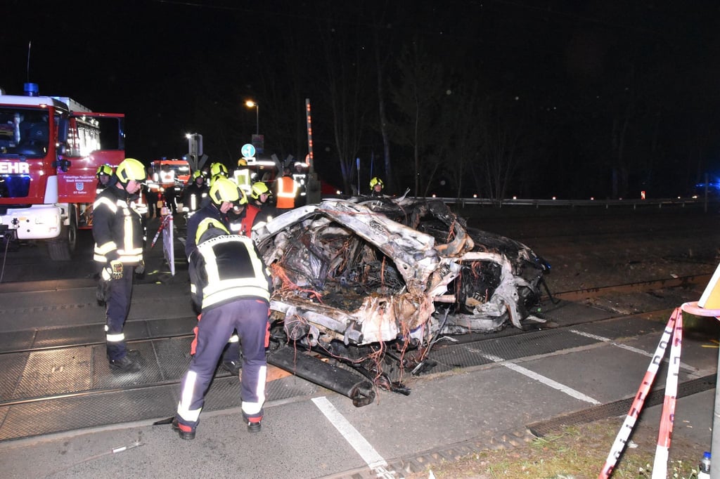 Rettungskräfte stehen am Wrack eines zerstörten Autos nach einem Unfall an einem Bahnübergang.