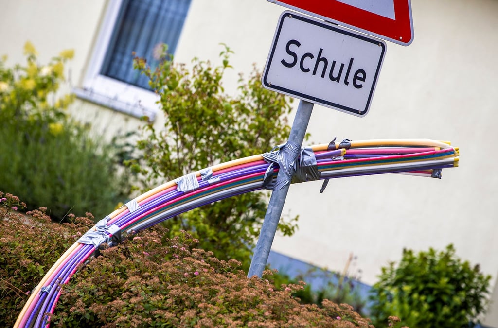 Leerrohre für das spätere Einblasen von Glasfaserkabeln hängen an einer der Baustellen an einem Hinweisschild für eine Schule.