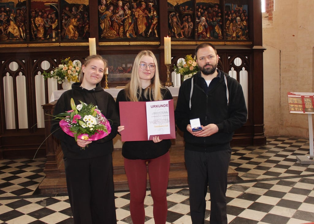 Charlotta Brauer und Seraphina Rudloff vom GutsMuthts-Gymnasium Quedlinburg freuen sich mit Elmar Egner, Leiter des Domschatzes Quedlinburg, über den Romanik-Preis 2023.