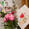Eine selbstgemalte Karte mit Herz steckt in einem Blumenstrauß, während auf einem Kühlschrank Fotos einer Familie hängen. (Foto:&nbsp;