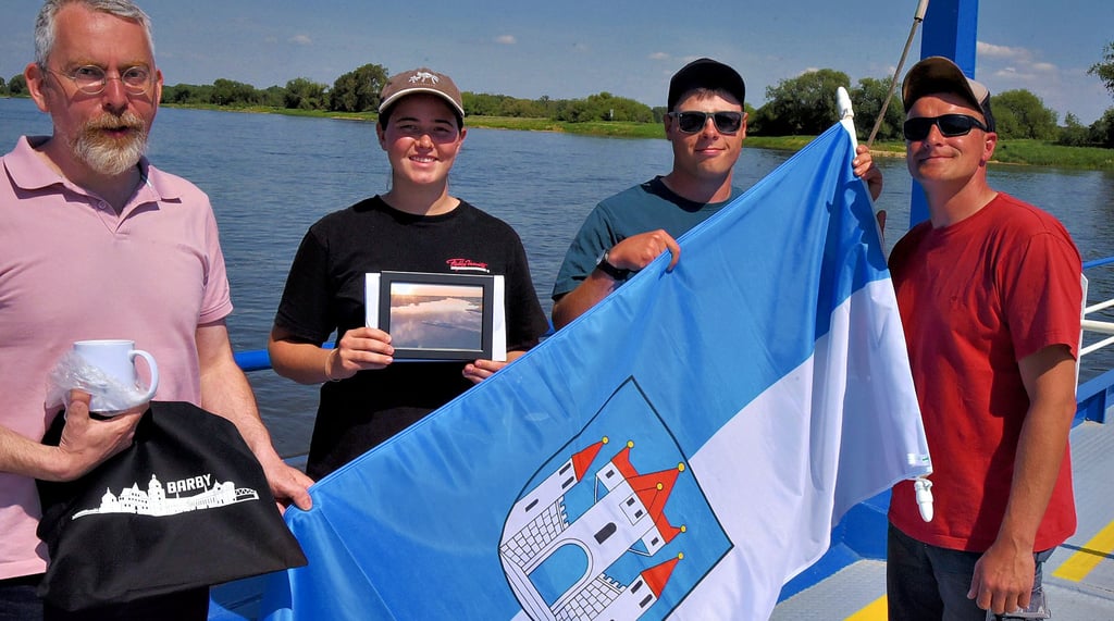 Geena Sadlowski, Praktikantin auf der Gierfähre Barby, stammt aus Namibia. Bürgermeister Jörn Weinert (l.) und die Fährmänner Hannes Tönnies und Stefan Teubner (r.) verabschiedeten sie an ihrem letzten Tag mit ein paar kleinen Barby-Souveniers.