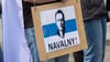 Ein Mann trägt ein Schild mit dem aufgedruckten Gesicht von dem gestorbenen Regimegegner Alexej Nawalny.