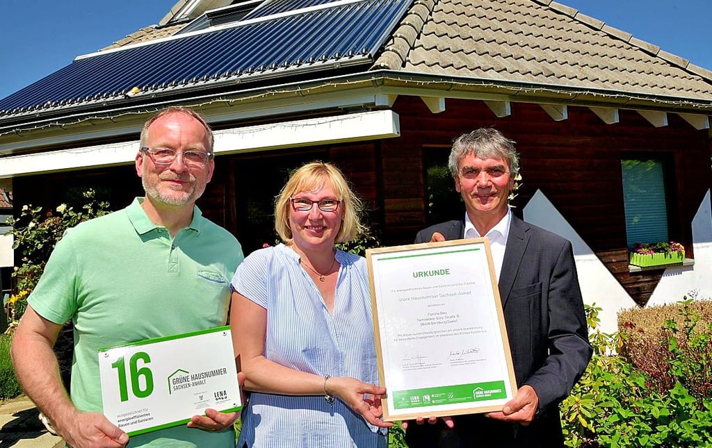 Staatssekretär Steffen Eichner (rechts) übergibt Annett und Mark Bley die erste „Grüne Hausnummer“ in Bernburg.
