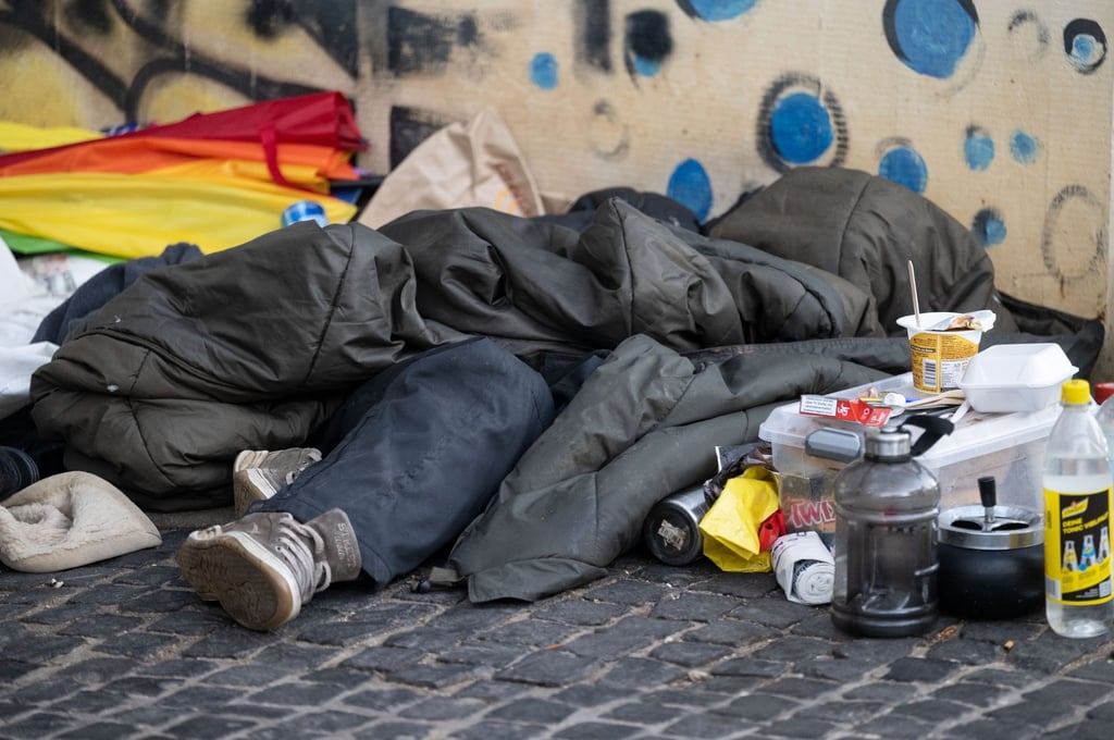 Eine Person liegt in der Innenstadt unter einem Schlafsack.